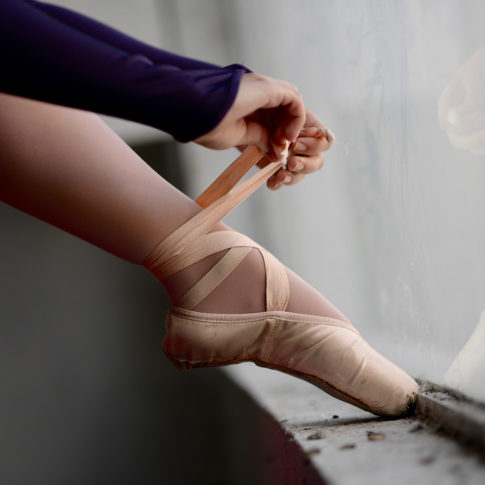 C'est une photo artistique avec de la lumière naturelle avec une danseuse qui se noue son chausson au rebord d'une fenêtre